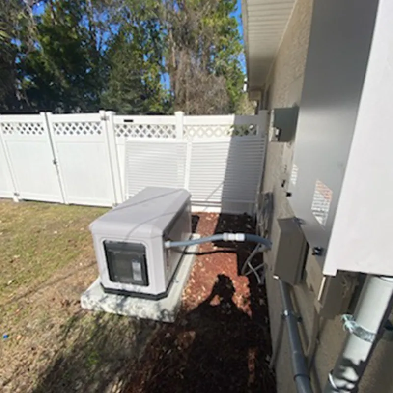 Standby generator on its pad beside a home, next to a white vinyl fence