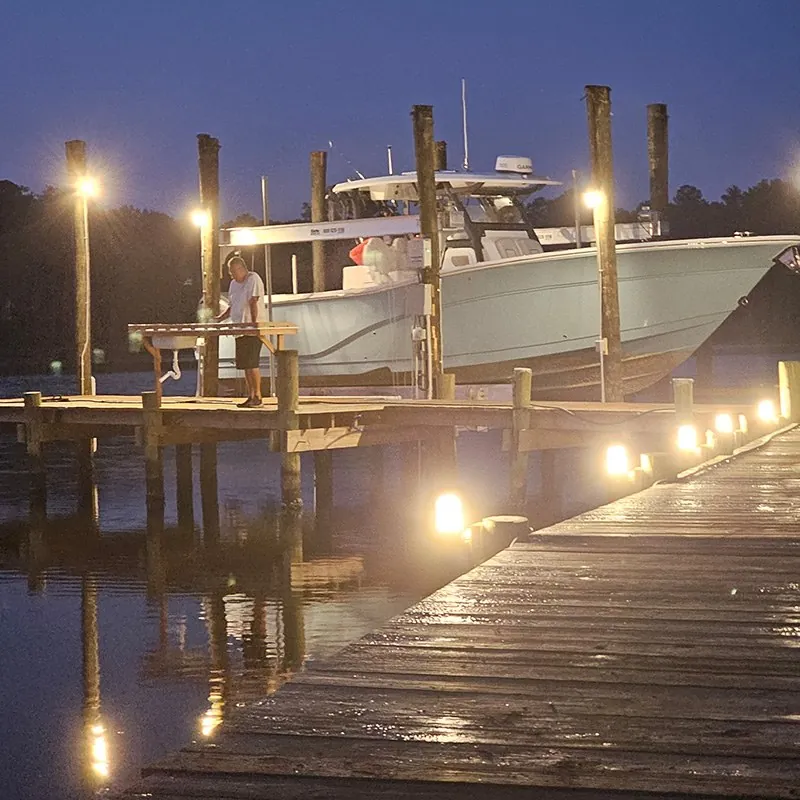 A center-console boat on its lift at a residential dock at dusk, with piling lights and low dock lights on