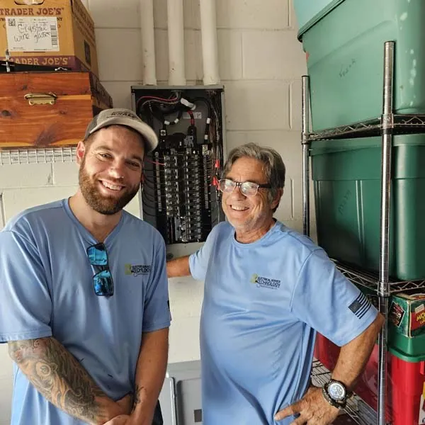 John and a crew member in a garage next to a panel they upgraded